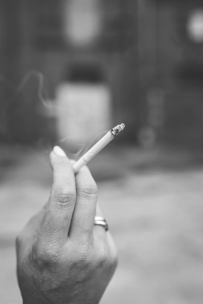 Black and white photo of a hand holding a cigarette with smoke rising.
