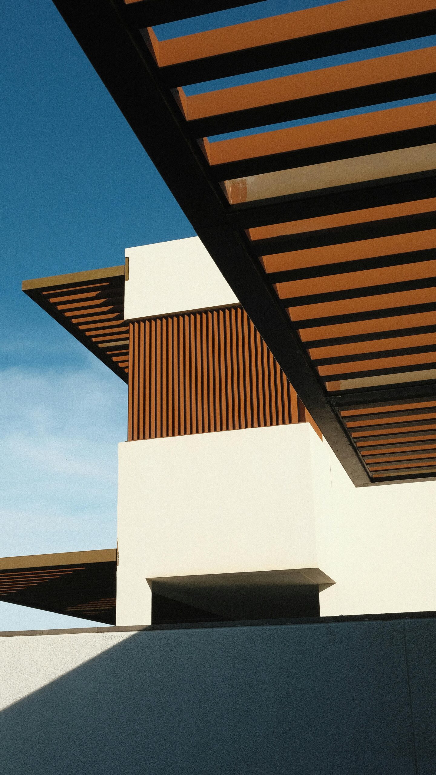 A contemporary building showcasing geometric design and wooden accents against a clear blue sky.